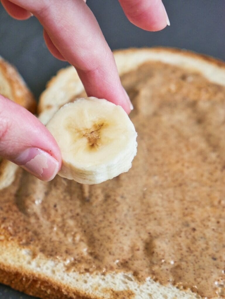 fingers putting banana slice on toast