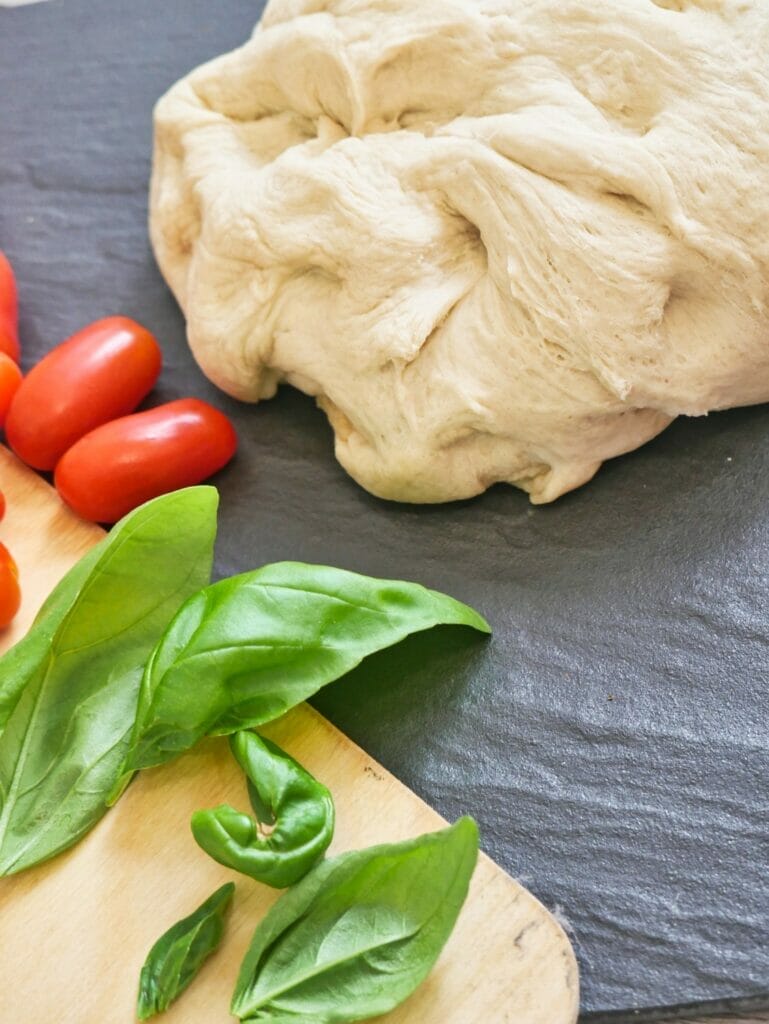 giant ball of uncooked pizza dough and basil leaves and tomatoes