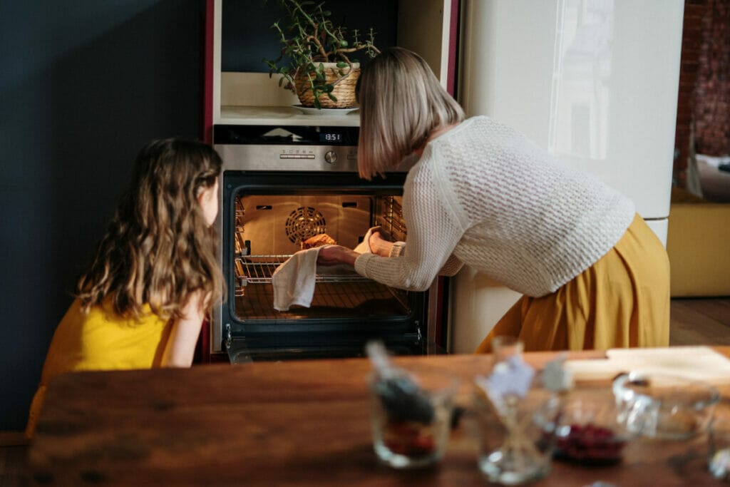 mom and daughter putting cookies in oven