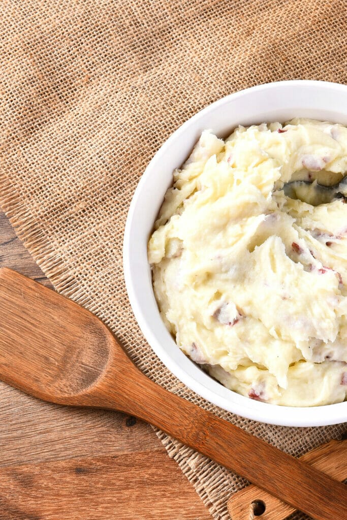 Wooden spoon next to a bowl of mashed potatoes 