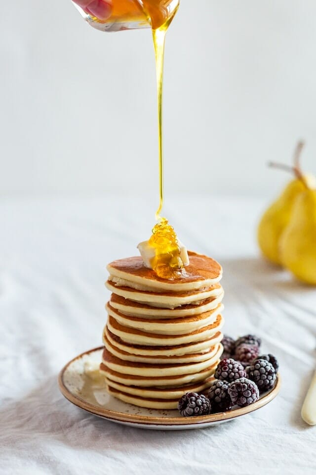 Syrup being poured on a stack of pancakes 