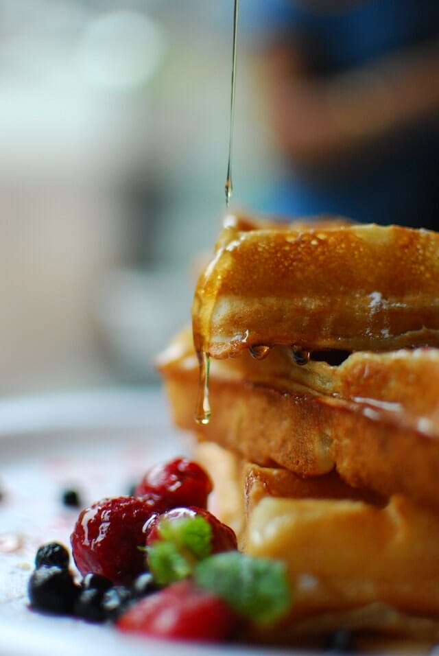 Waffles getting syrup poured on them with berries 